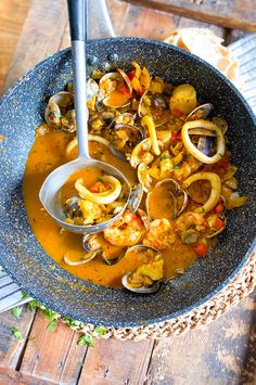 a bowl filled with soup and clams on top of a wooden table next to a spoon