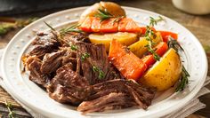 a white plate topped with roast, potatoes and carrots