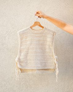 a woman holding up a white crochet top with tassels on it