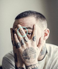 a tattooed man covering his face with both hands and looking at the camera while holding his hand to his face