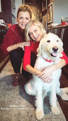 two women and a white dog posing for a photo in the living room with their arms around each other