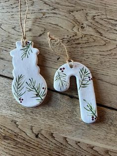 two wooden ornaments with pine branches and berries hanging from strings on a wood surface,