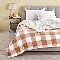 a bed with white and brown checkered blankets on it, next to a night stand