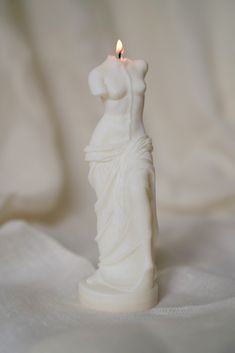 a white candle that has a statue on it with a lit candle in the middle