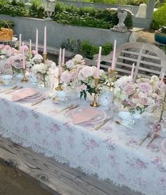 the table is set with pink and white flowers, candles, and plates on it