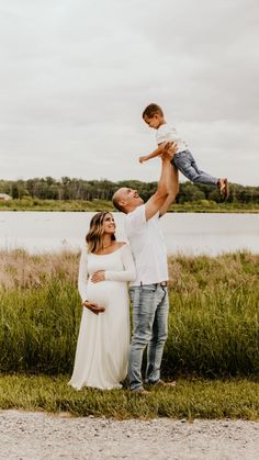 a man holding up a baby while standing next to a woman in a white dress