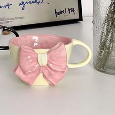 a coffee cup with a pink bow on it next to a glass vase and sign