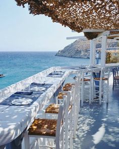 an outdoor dining area with tables and chairs near the water, under a pergolated roof