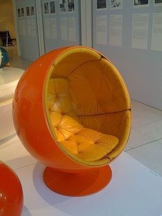 an orange chair sitting on top of a white floor next to two red balls and chairs