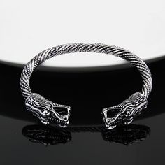 a silver bracelet with an intricate design on the front and back ends, sitting on a black surface