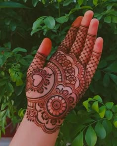 a hand with henna on it and some plants in the backgrouf