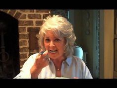 an older woman is brushing her teeth in front of a brick wall and fireplace,