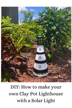 a white and black light house sitting in the middle of a garden with plants around it