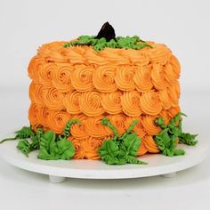 a cake with orange icing and green leaves on a white platter against a white background