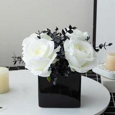 a black vase with white flowers on a table next to two candles and a mirror