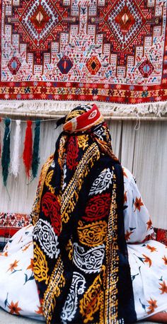 a person sitting on the ground in front of some rugs and other items that are hanging up