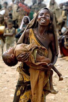 a woman carrying a child on her back in front of a group of other people