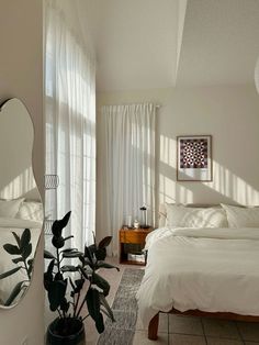 a bed room with a neatly made bed next to a mirror and potted plant