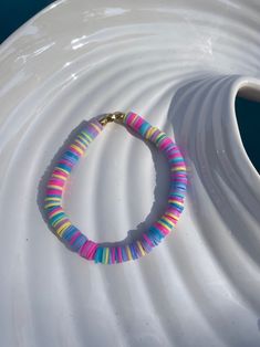 a bracelet with multicolored beads is sitting on a white vase