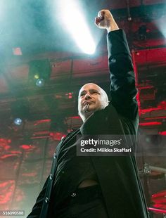 a man in black jacket standing on stage raising his fist up to the sky with lights behind him