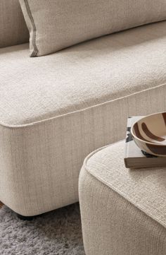 a close up of a bowl on a table near a couch with pillows and a book