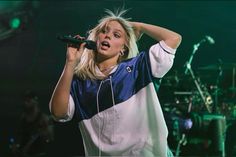 a woman holding a microphone up to her ear while standing in front of a band