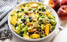 a white bowl filled with salad next to two peaches