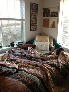 an unmade bed sitting in front of two windows next to a window sill