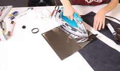 a woman is ironing fabric with an iron on the table next to her bag