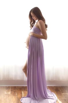 a pregnant woman in a purple dress standing on a wooden floor with her belly exposed