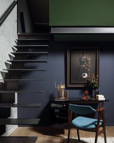 a blue chair sitting in front of a desk under a stair case next to a painting on the wall