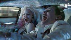 two people sitting in the back seat of a car, one with pink hair and another with green eyes