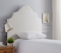 a white headboard with pillows on top of it in a bedroom next to a lamp