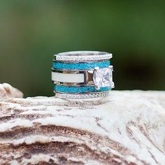 two wedding rings with blue and white glitter on them sitting on a piece of rock