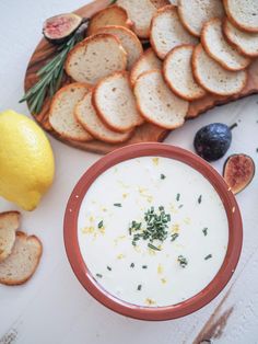 a bowl of yogurt surrounded by sliced bread, olives and lemon slices