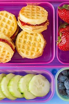 a lunch tray with waffles, fruit and cucumber slices on it