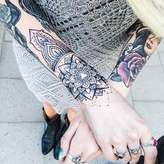 two people holding hands with tattoos on their arms and fingers, both wearing rings that have flowers on them