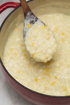 a wooden spoon in a red pan filled with corn and grits on a white counter