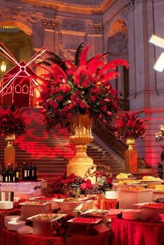 a banquet table with red cloths and flowers on it in front of a staircase