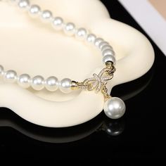 Embark on a journey of sophistication with our Bridal Pearl Earring and Necklace Set, where timeless elegance meets modern sparkle. This exquisite pearl jewelry set centers around a 10mm white pearl, renowned for its classic beauty and radiant glow. Representing centuries of elegance, the pearl is perfectly complemented by the set's contemporary design, making it an ideal choice for brides or anyone looking to add a touch of refined glamour to their ensemble. Delicate Glamour: Chic Bow Pendant O