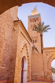 an archway leading to a building with a clock tower in the background and palm trees on either side