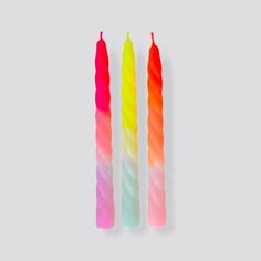 three multicolored candles sitting next to each other on a white surface with one candle in the middle