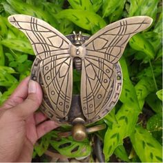 a hand holding a butterfly shaped object in front of some plants