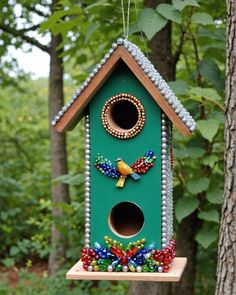 a green birdhouse with beads hanging from it's side in front of trees