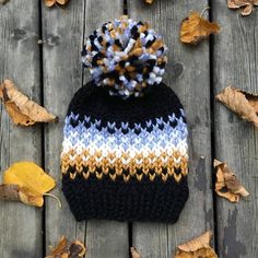 a knitted hat sitting on top of a wooden table next to leaves and fallen leaves