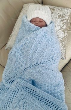 a baby wrapped up in a blue blanket on top of a white couch next to pillows