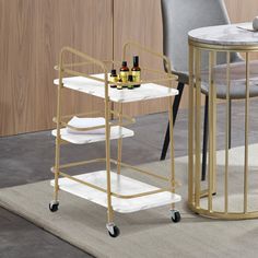 a gold bar cart with two bottles on it next to a gray chair and table