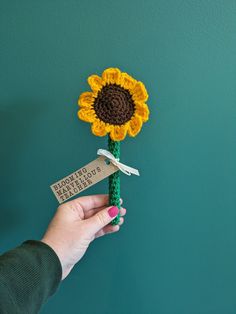 a hand holding a crocheted sunflower on a green wall