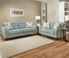 a living room with two blue couches and a white rug on the wooden floor