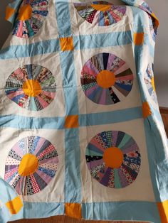 a blue and white quilt with orange circles on it sitting on a wooden floor next to a wall